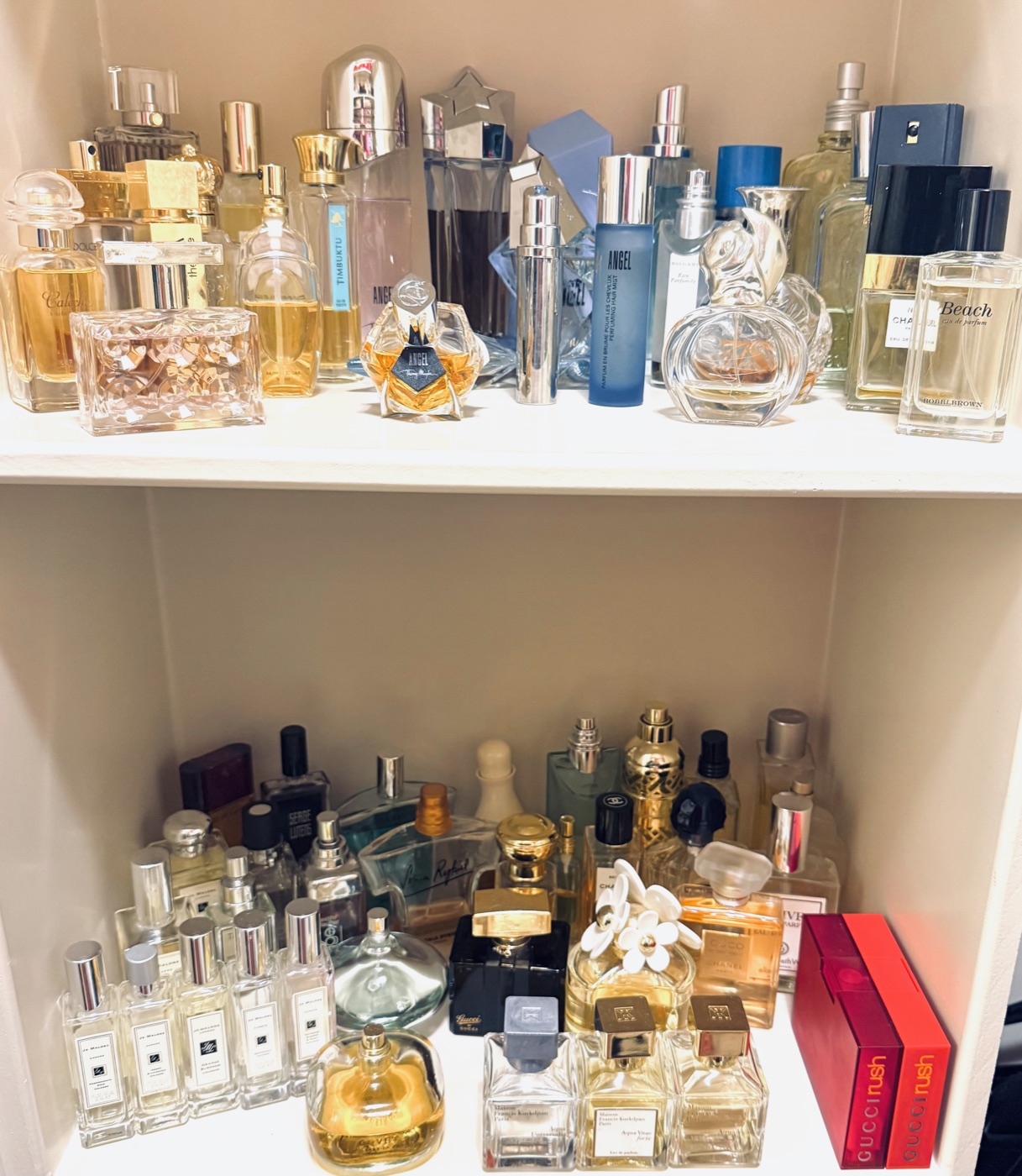 Designer perfume and fragrance collection organized on white shelving